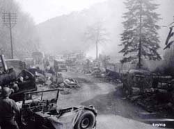 Amerikanische Militärwagen fahren durch ein zerstörtes Dorf.