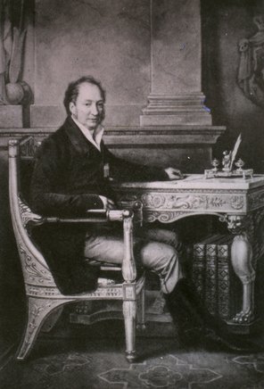 Porträt des bayrischen Königs Max I. Josef, schwarzweiß, von der Seite abgebildet, an einem Schreibtisch sitzend.