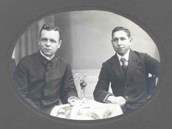 Photographie der jungen Brüder Albert und Johannes Finck an einem kleinen Tisch sitzend, darauf ein Weinglass. Johannes trägt Pfarrerhabit, Albert Anzug.