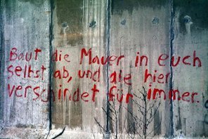 Bild eines Abschnitts der Berliner Mauer, darauf ein rotes Graffiti: Baut die Mauer in euch selbst ab und die hier verschwindet für immer.