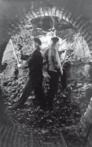 Schwarz-weiß Photographie zweier Bergleute mit Spitzhacken im Stollen.